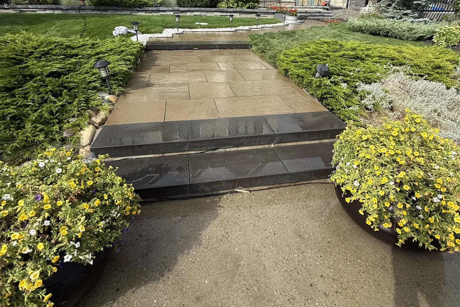 Stone paver walkway with dark granite steps, landscape lighting, and flowering garden beds, Calgary hardscaping by All The Moore