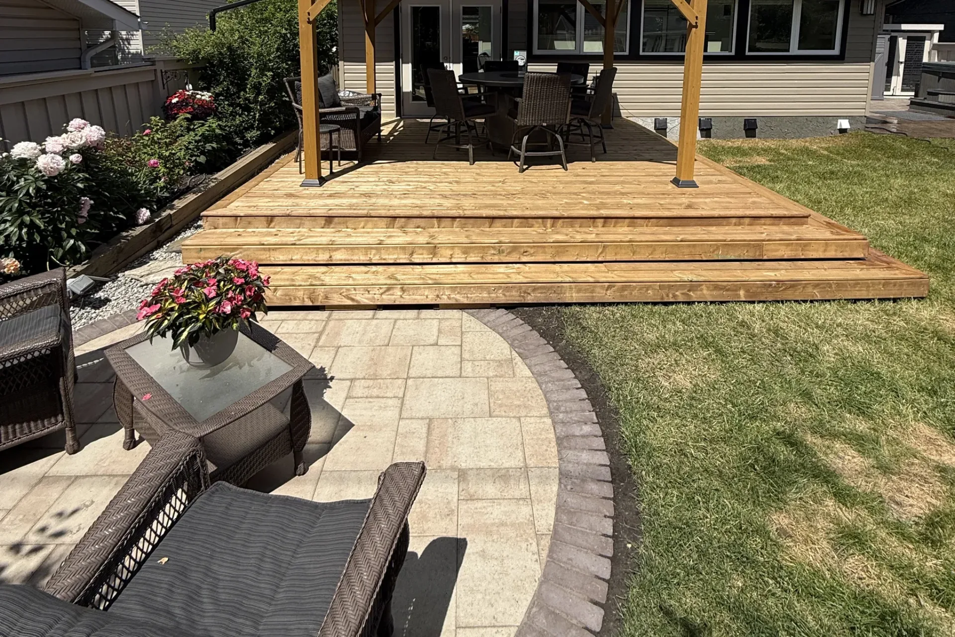 Cedar deck with timber pergola, curved interlocking paver patio, wicker outdoor furniture, and garden beds, Calgary by All The Moore