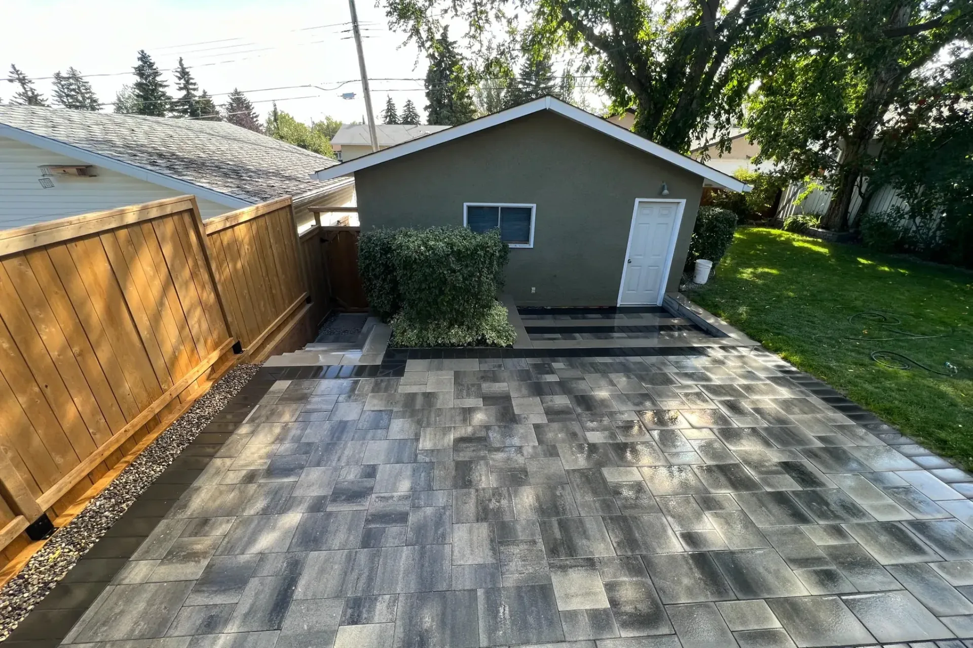 Black interlocking paver driveway with garage and cedar privacy fence, Calgary hardscaping by All The Moore Landscaping