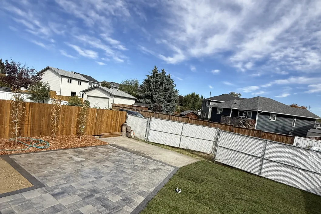 Completed Calgary backyard with large interlocking paver patio, fresh sod, and cedar fence by All The Moore Landscaping