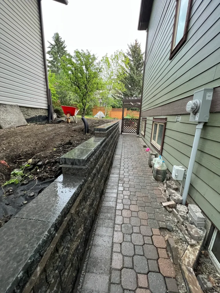 A narrow pathway leads between two houses lined with stone and greenery