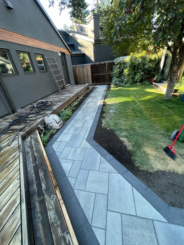 Stone paver walkway next to multiple dark wooden decks on a residential home.