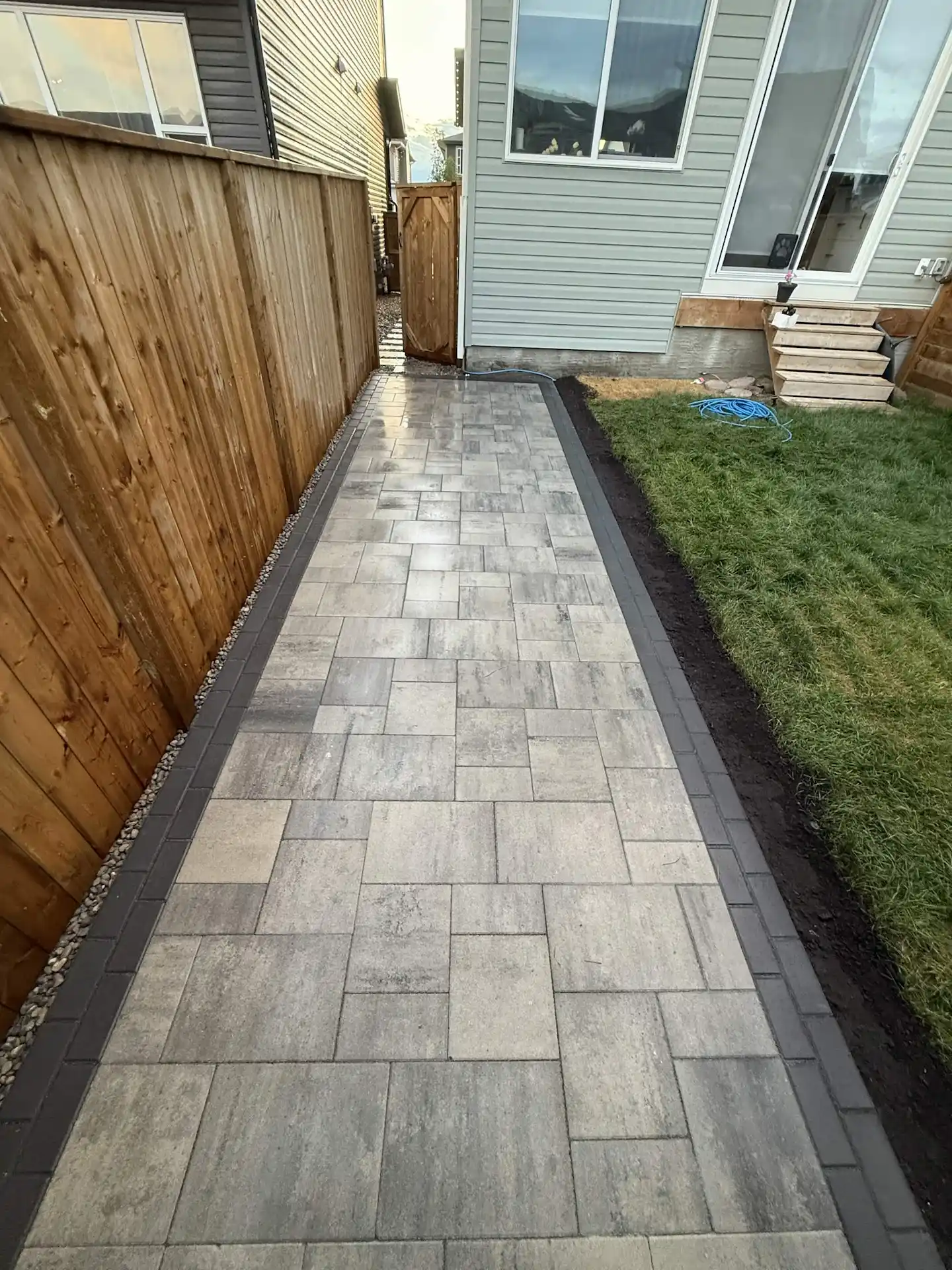 A newly laid stone pathway leads through a narrow yard, bordered by wooden fences